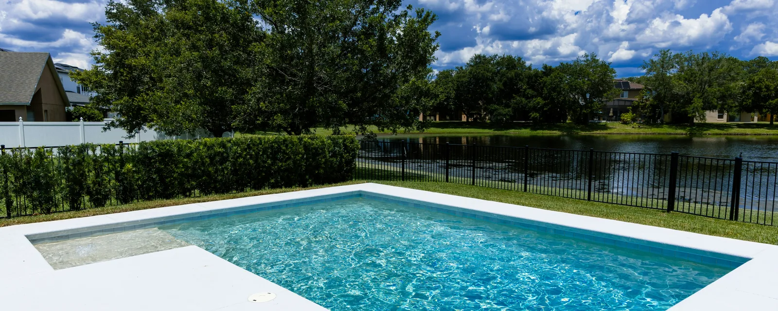 Rectangular inground pool with white concrete coping in a fenced backyard overlooking a lake