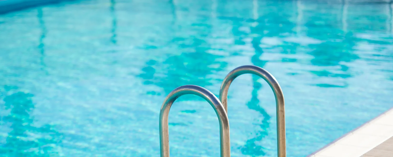 Stainless steel handrail at the edge of a bright turquoise inground pool