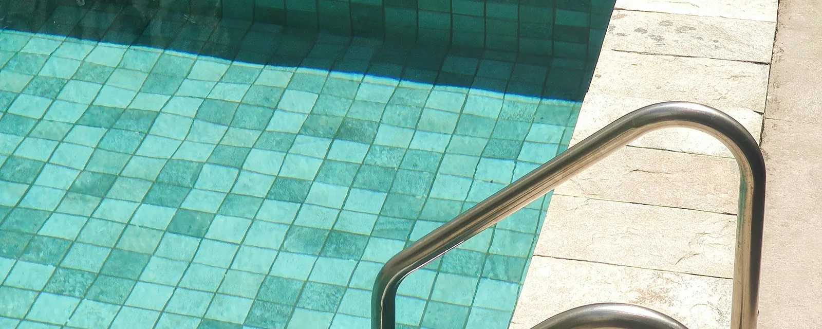Tiled steps and handrail leading into an inground pool with stone coping